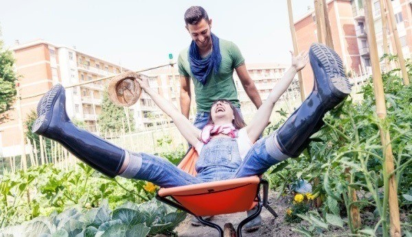 man pushing woman in wheelbarrow through garden