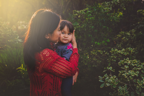 A pretty mom holding her sweet toddler girl outdoors in the woods.