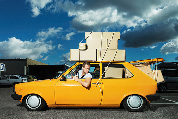 young man driving with boxes tied to the roof of his car