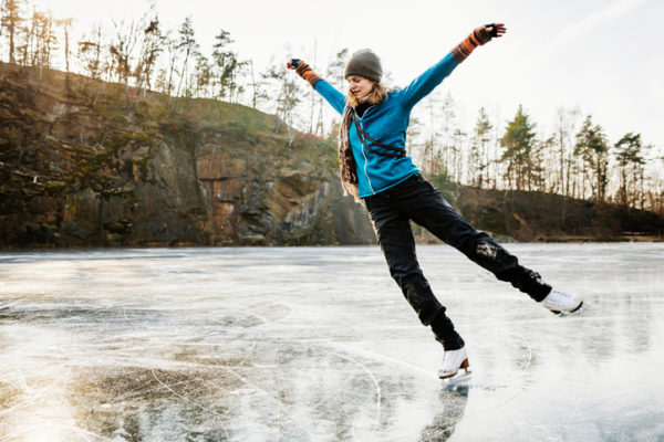 An amateur ice skater posing with her arms in the air while skating on a frozen lake.