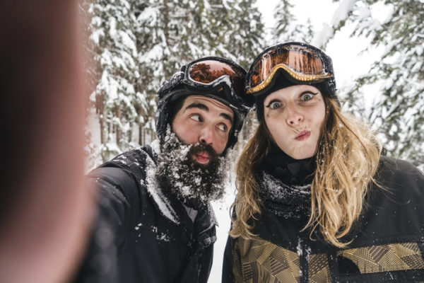 Selfie of happy couple in skiwear grimacing in winter forest