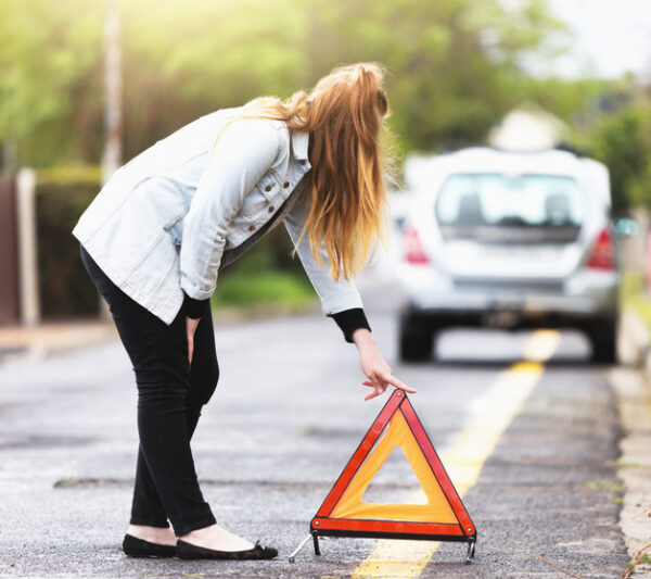 A young redhead bends to place a hazard warning triangle behind her car which has broken down.