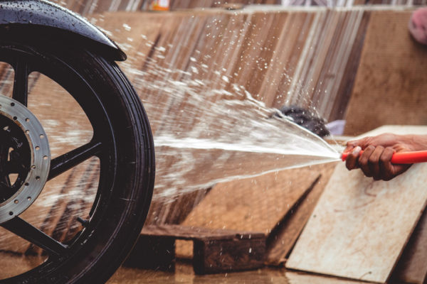 Cropped Hand Spraying Water On Motorcycle Tire