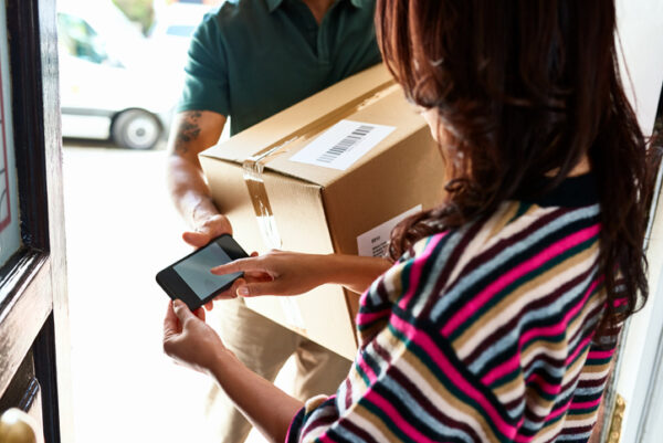 Female customer at front door holding smartphone and receiving package from delivery man, service, identity, online shopping