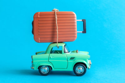 Suitcase on car roof on blue background minimal creative travel concept.