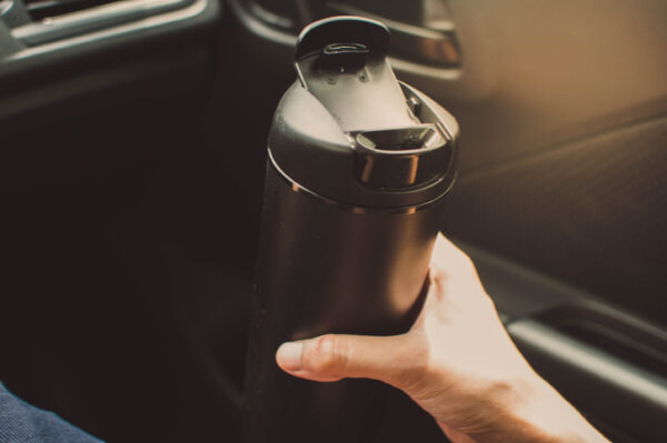 A young person is drinking from a reusable beverage mug while inside the car