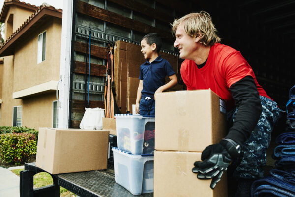 Smiling young boy standing in back of moving truck while mover picks up boxes