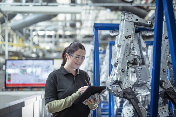 Female apprentice engineer using digital tablet to inspect parts in car factory