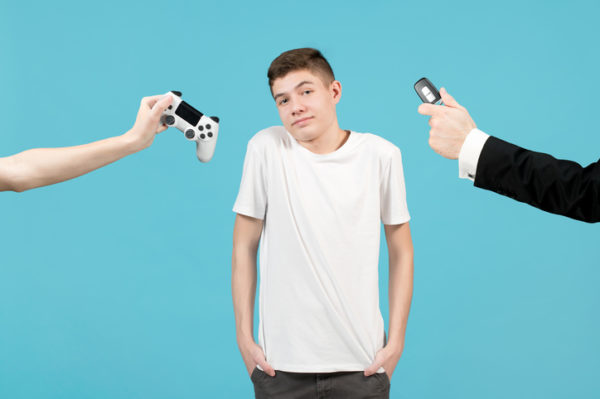 a young man is offered a choice of driving a car or playing a console. Hands holding out a car key and a joystick