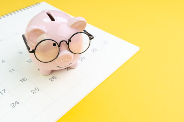 Annual budget allocation, schedule for saving and invest or planning for financial date, smiling pink piggy bank wearing eyeglasses on white clean calendar on solid yellow background with copy space.