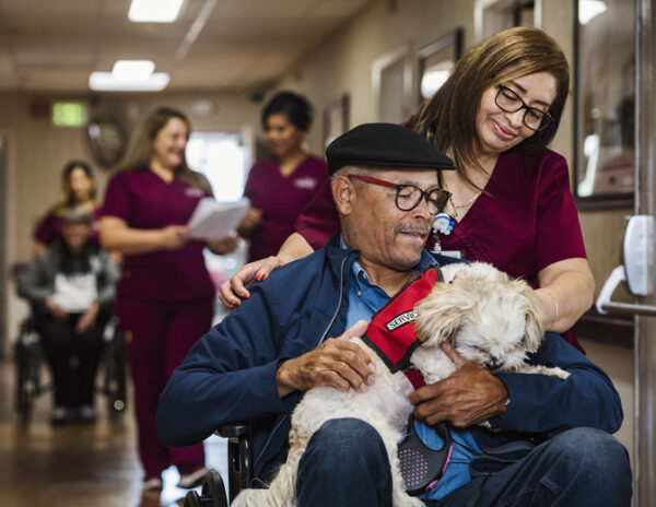 Nurse assisting senior man in wheelchair holding service dog