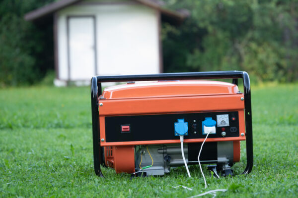 Portable electric generator with white electric wires on the backyard of a summer house outdoors. The generator provides the house with electricity