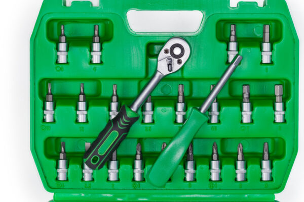 Ratchet handle and screwdriver for interchangeable heads lie on a set of bits different shapes and sizes in the green plastic toolbox, top view
