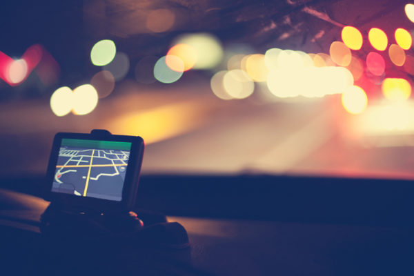 Night shot of GPS navigational system on dashboard of car. Traffic lights are visible through windshield.