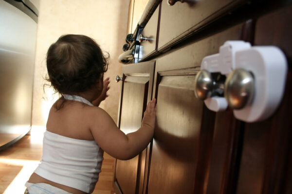 Toddler cruising along the kitchen - part of a series - focus on unsecured cabinet door