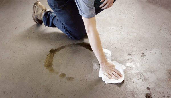 Oil clean-up in a workshop. A man cleaning-up an oil spill on a workshop floor. The man is wearing work boots and mechanic's clothing.