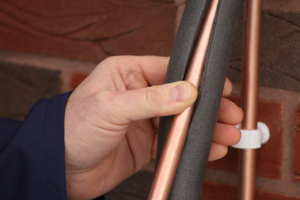 "Plumber applying insulation to copper water pipes,focus on insulation."