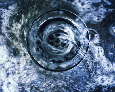 Water spiraling down a plug hole in stainless steel kitchen sink drain with soap suds and bubbles