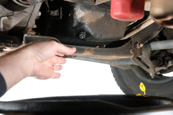 "Hand reaching for engine oil drain plug under car, horizontal with copy space."