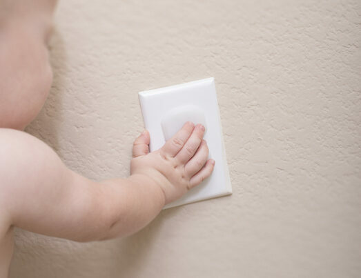 A baby reaching for a power socket but the power socket is protected by a child proof power socket cover.