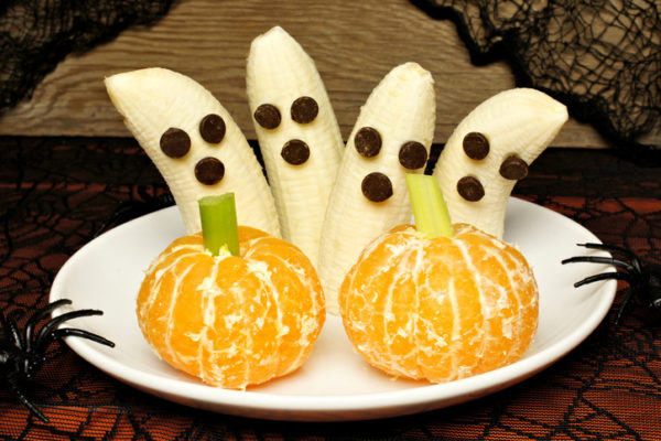 Healthy Halloween treats, banana ghosts and orange pumpkins, on a plate with holiday decor