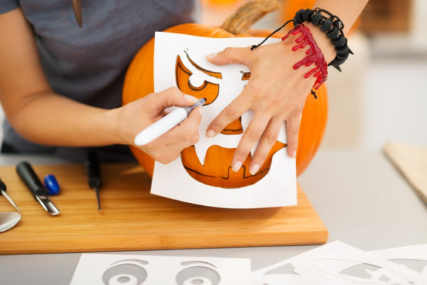 Closeup on woman using stencils to carve big orange pumpkin Jack-O-Lantern for Halloween party. Traditional autumn holiday