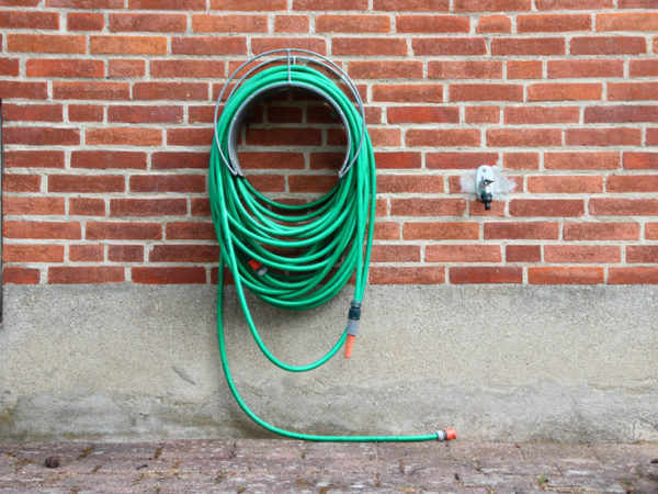 Green Garden Water Hose Hanging on Red Brickwall. Not connected to Water Tap.