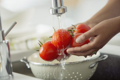 Mid-adult woman rinsing tomatoes in sink with colander.