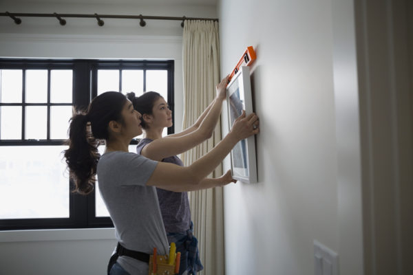 two women hanging picture frame on wall