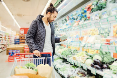 Young Man Groceries Shopping. Standing in front of produce stand and choosing salad