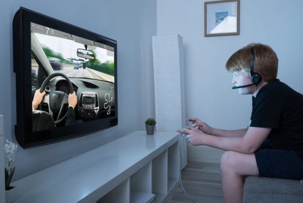 Boy With Joystick Playing Car Game On Television At Home