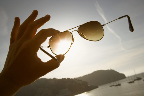 hand holding aviator sunglasses up against the sky