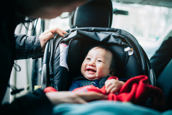 Close up of mother taking care of cute smiling baby on car seat in car