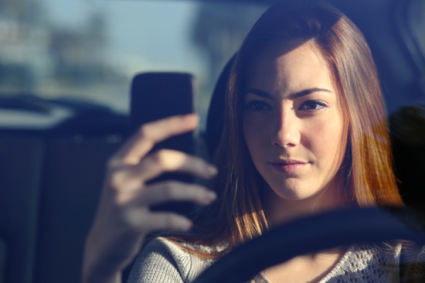 Front view of woman driving and typing on smart phone