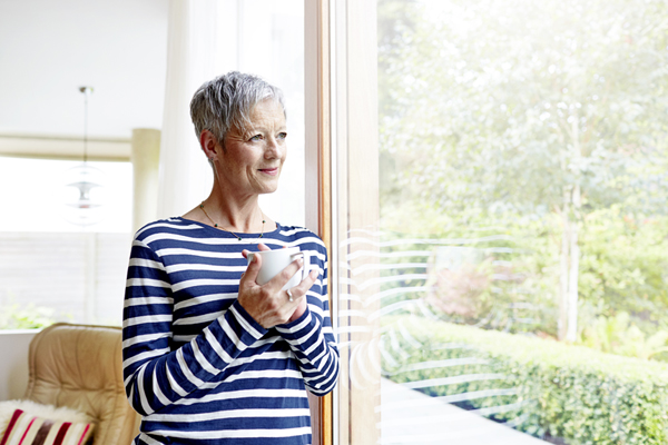 Older woman looking out window holding coffee mug