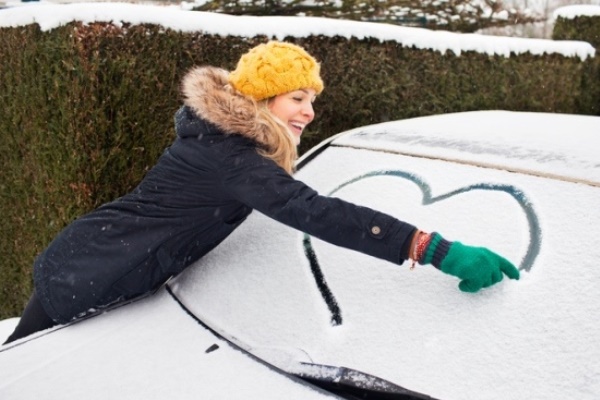 young woman drawing heart in show on car windshield