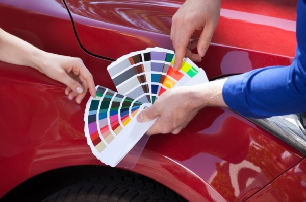 Mechanic Showing Color Samples To Customer Against Car