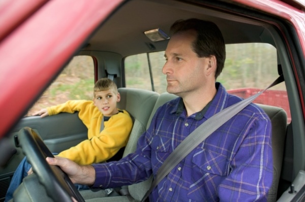 A boy looks at his father while he drives the truck.